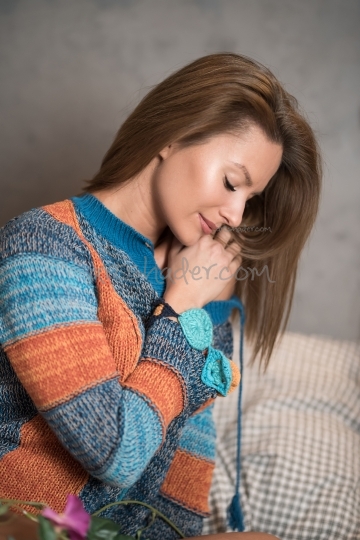Portrait of a woman sitting on a bed and wearing a sweater