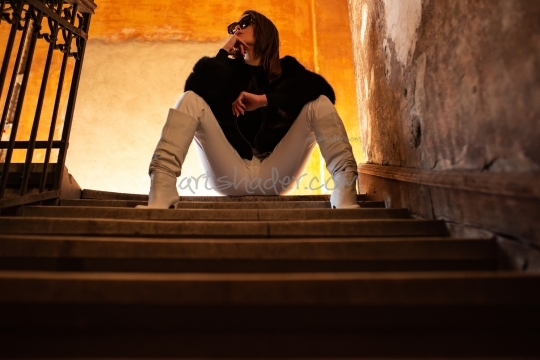 Young woman sitting on the stairs in a staircase at worn wall background.